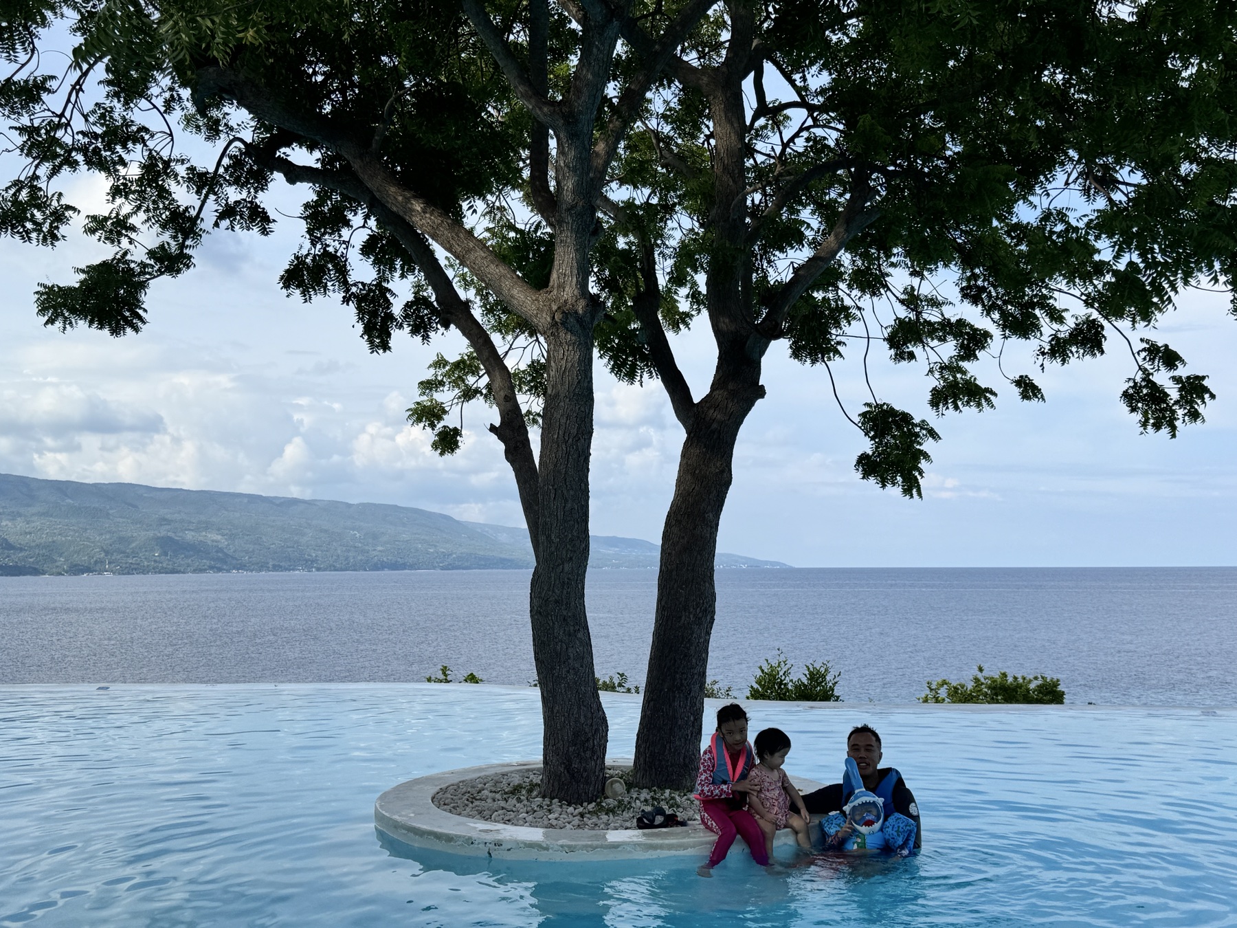 Philip and the children in the pool beneath a large tree with the Cebu coast beyond
