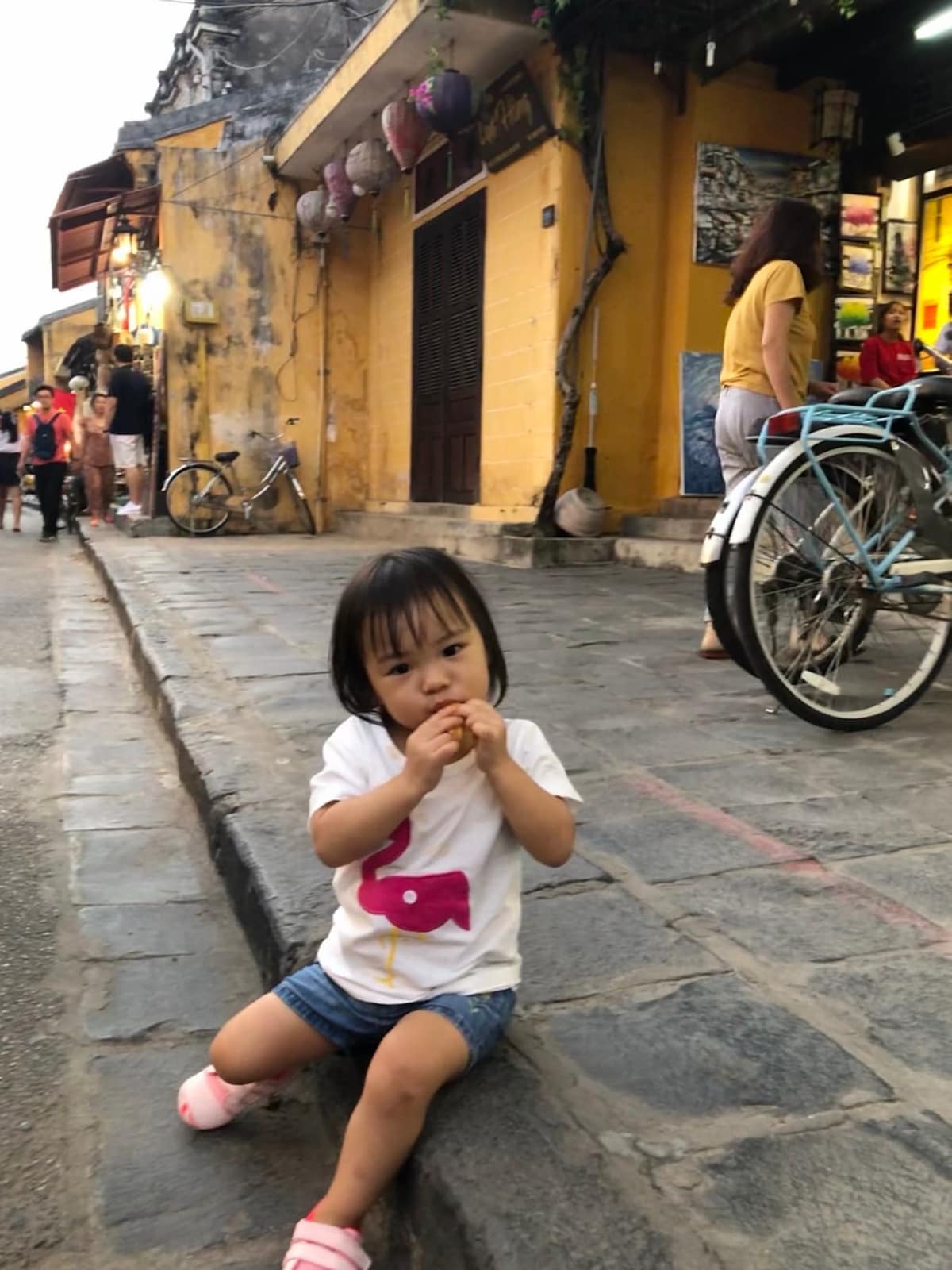 Sophie sitting on a stone street among Hoi An’s yellow walls and bicycles
