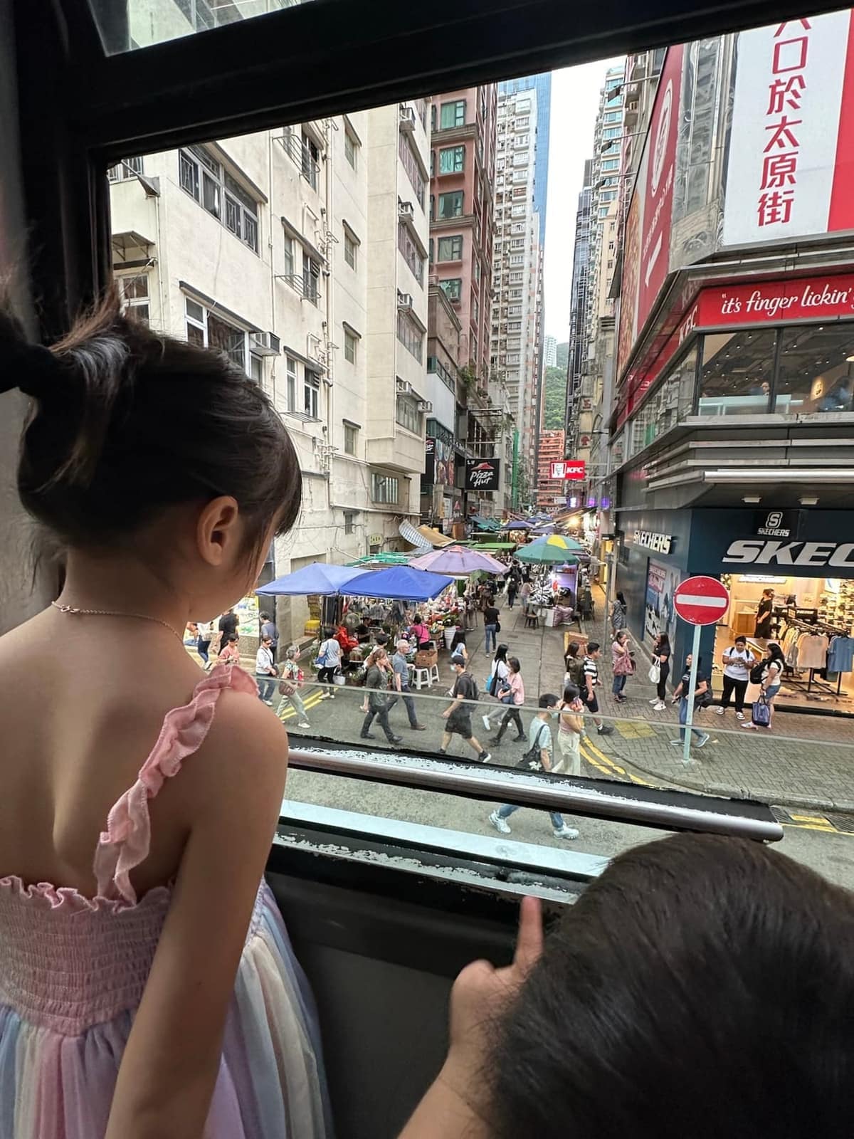 A child looking down at the street from the upper deck of a Hong Kong tram