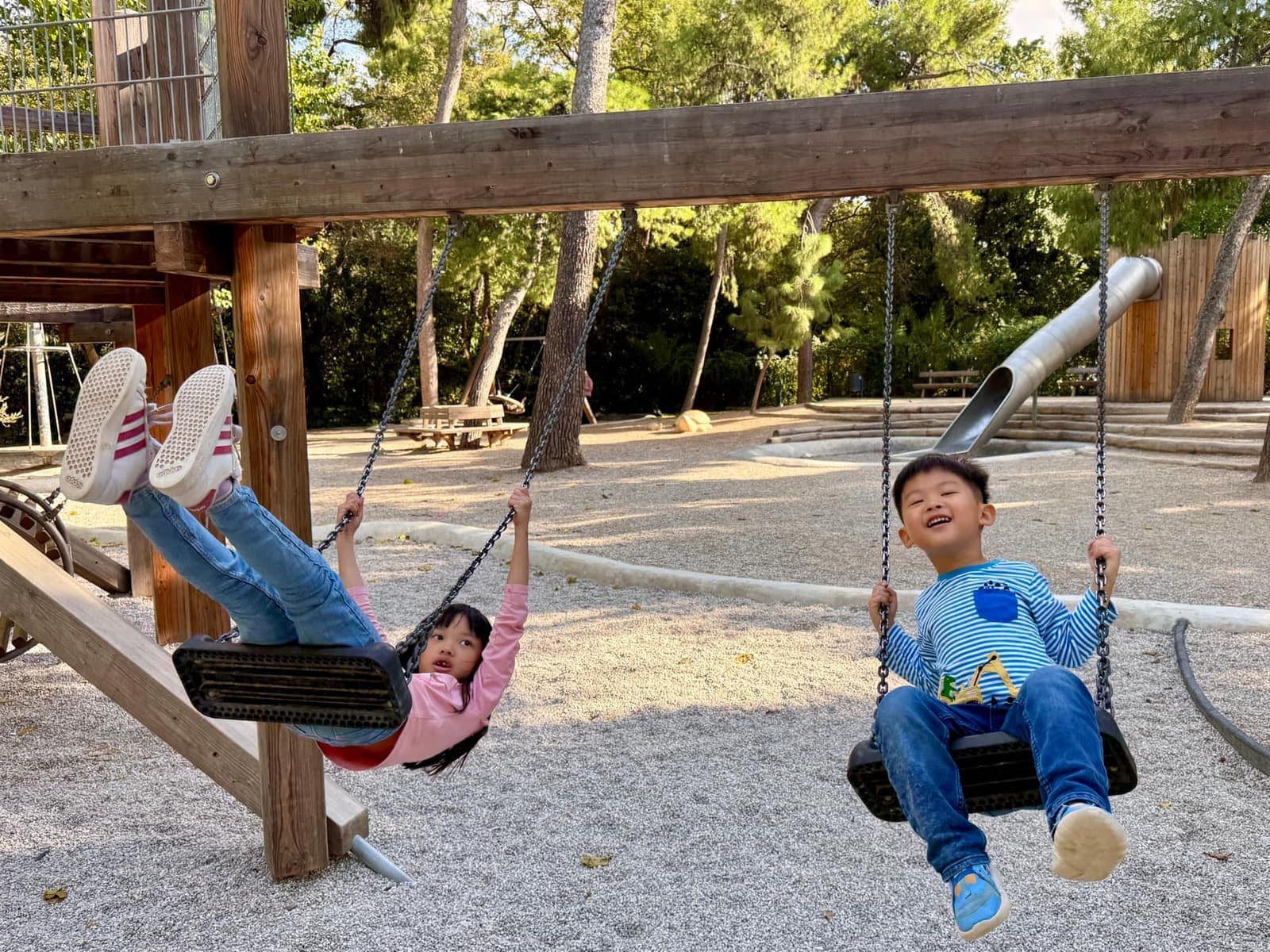 Sophie and George swinging together in a wooded Athens playground