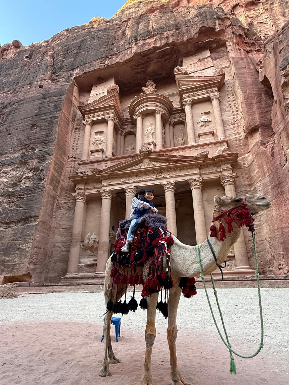 Sophie and George riding a camel in front of the Treasury at Petra