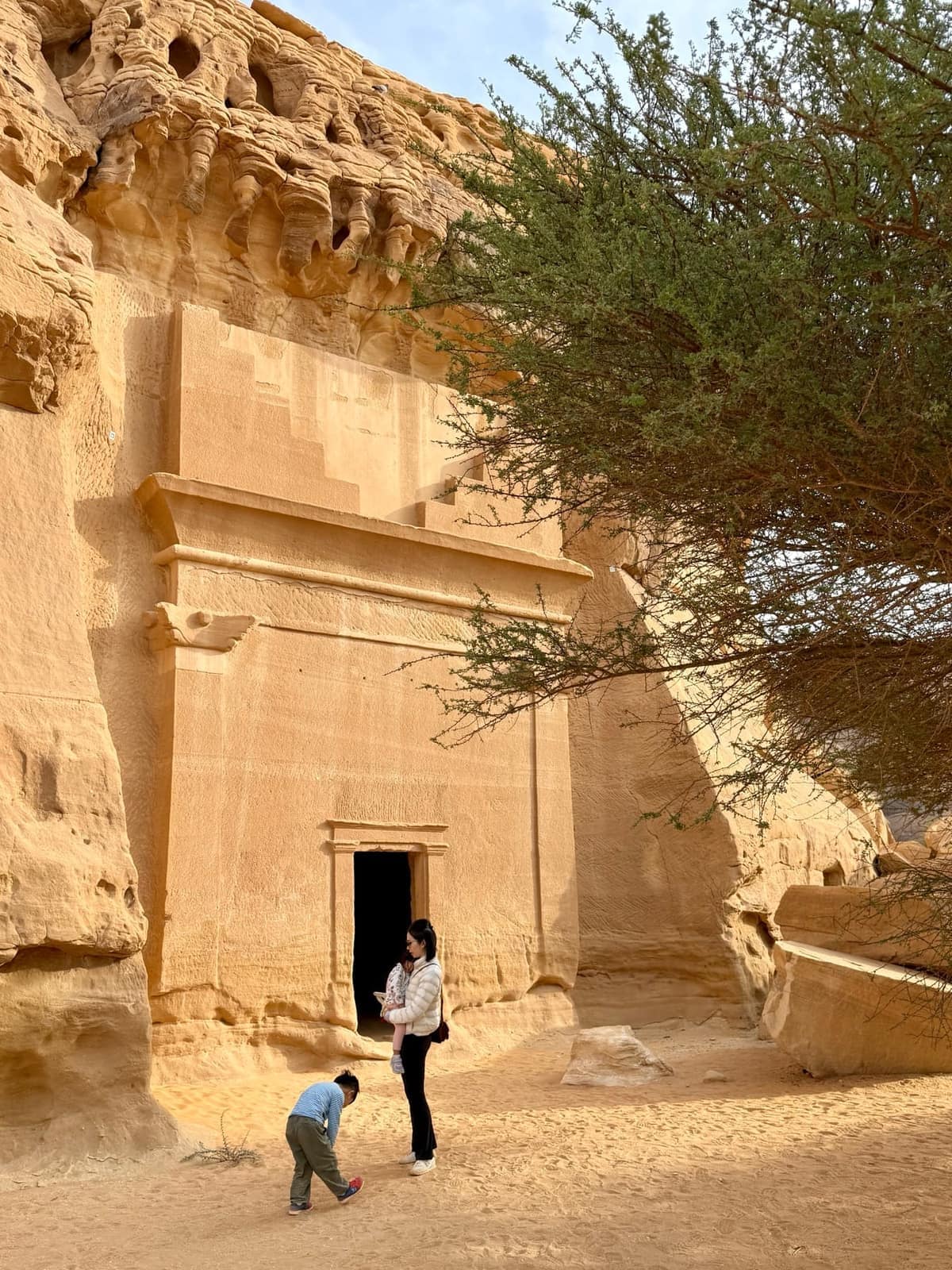 Vanessa waiting while George examines the sand beside a rock-cut tomb at Hegra