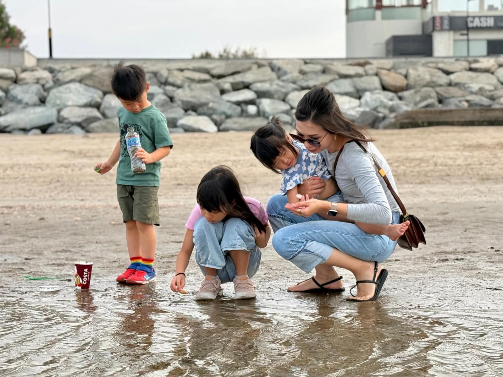 Vanessa and the children crouching together at shallow water in Muscat