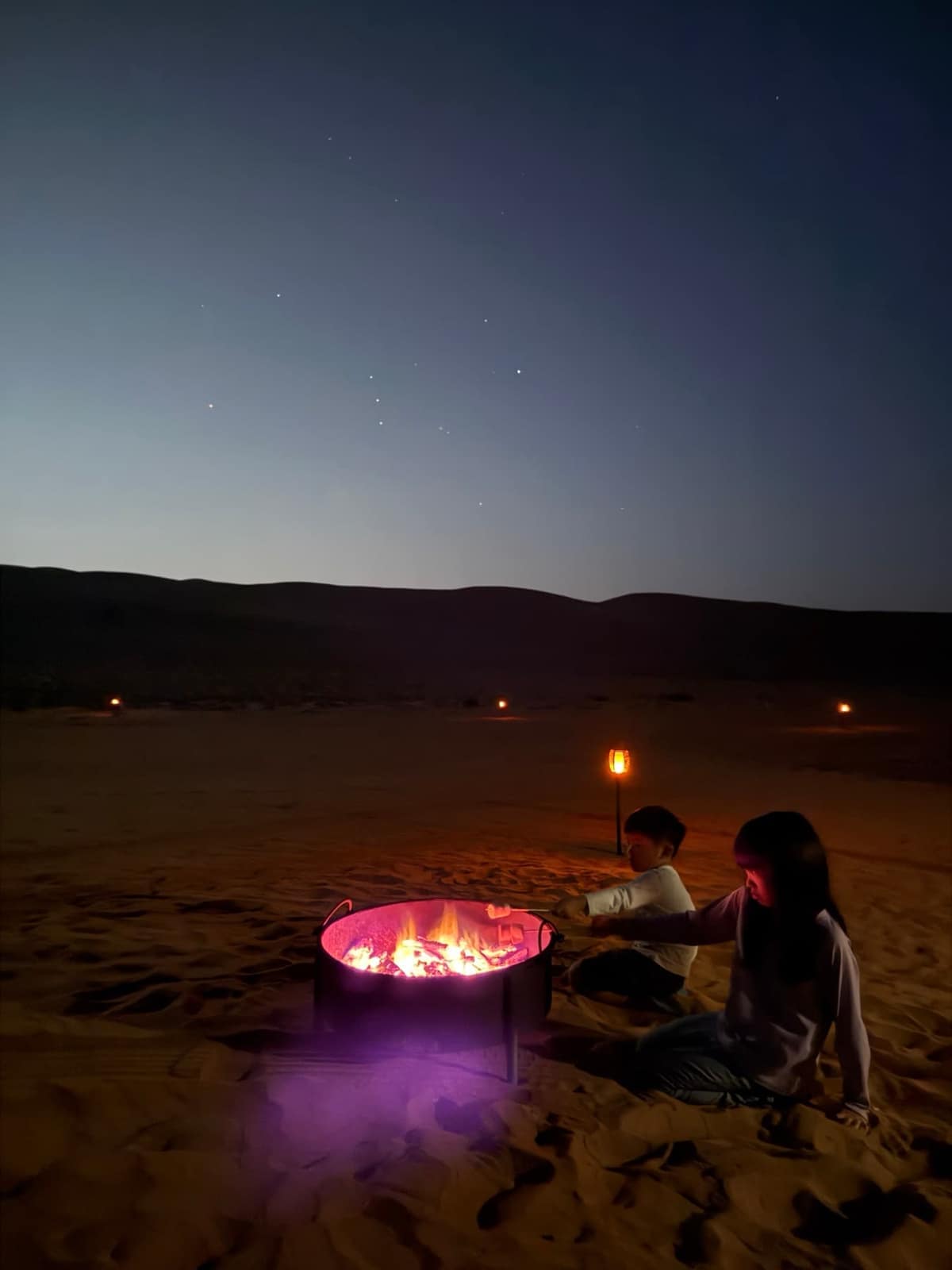 Sophie and George roasting marshmallows over a fire beneath the stars in Wahiba Sands