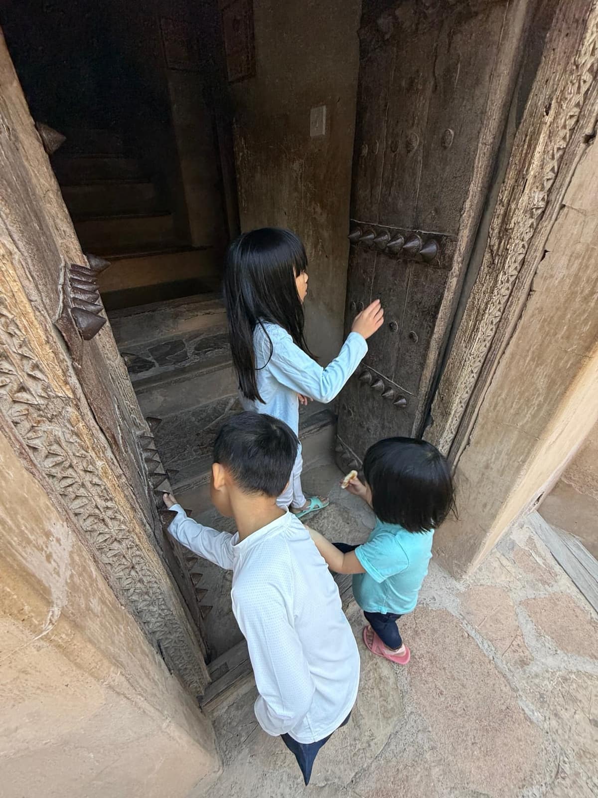 The children examining a heavy carved wooden doorway at Nizwa Fort