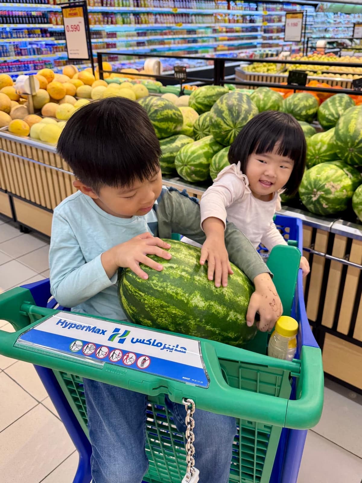 George and Claire handling a watermelon in a supermarket trolley