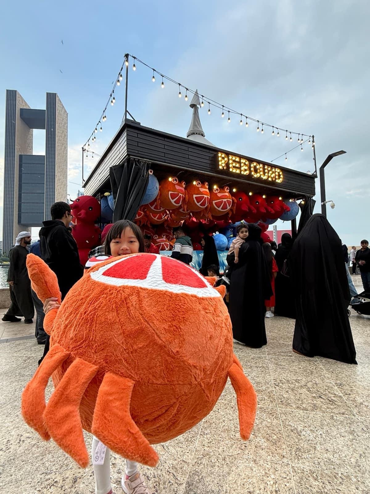 Sophie holding an enormous orange crab prize in front of a fairground game in Bahrain