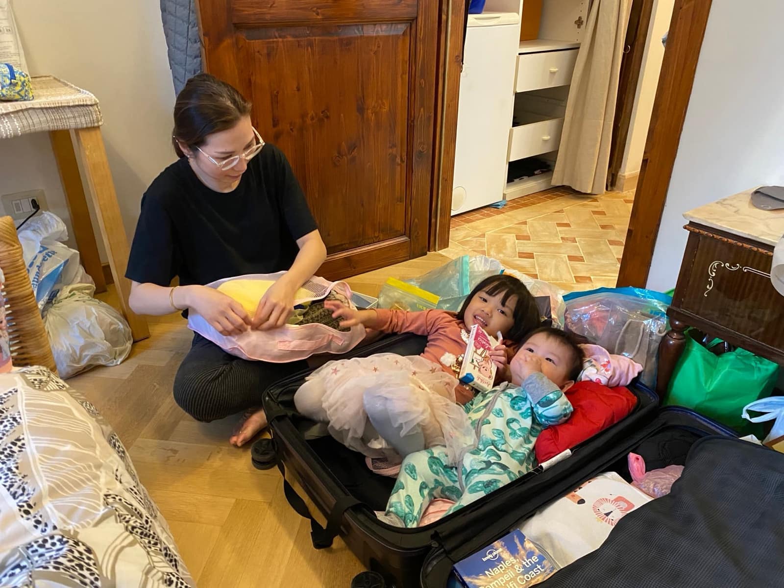 Sophie and George jumping into a suitcase while Vanessa packs