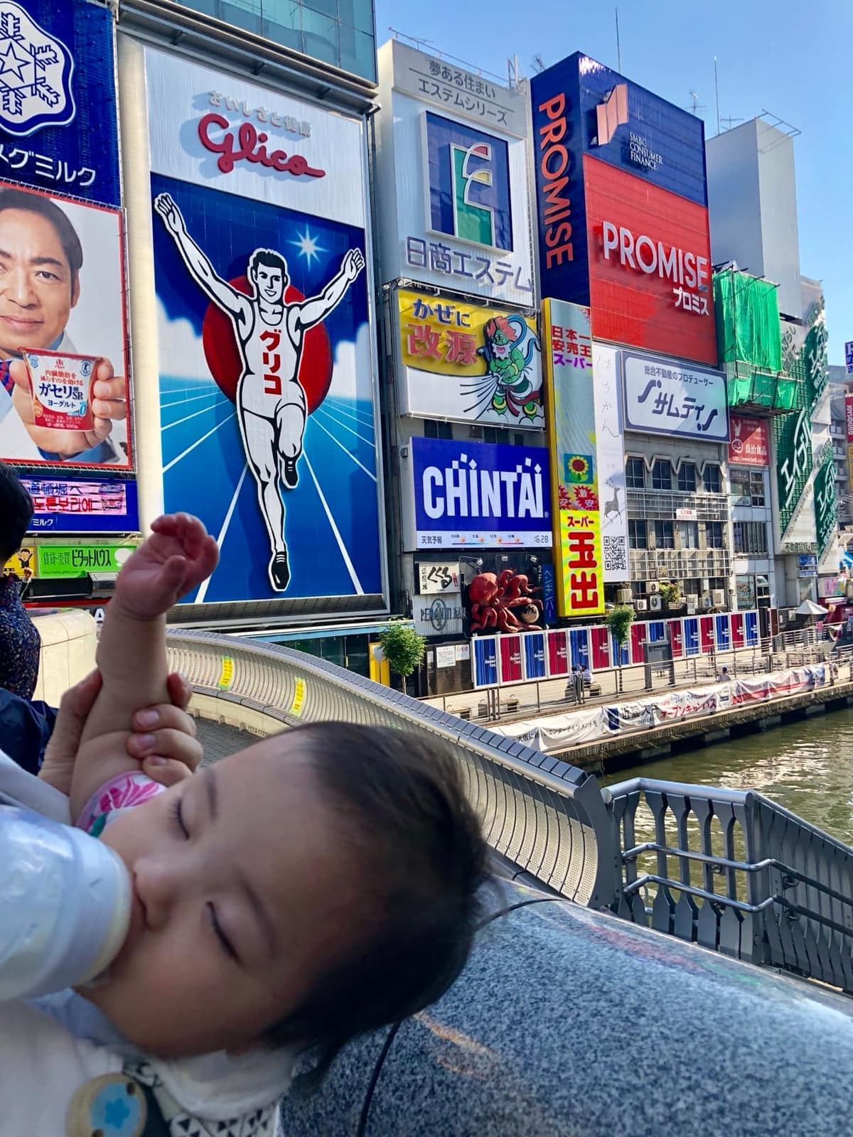 Sophie asleep in her stroller with the Glico running man above Dotonbori