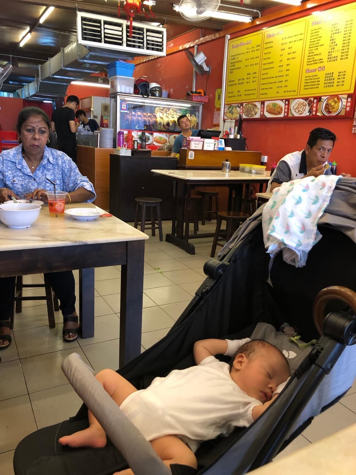 Sophie asleep in her stroller while the family eats at a casual restaurant in Malacca