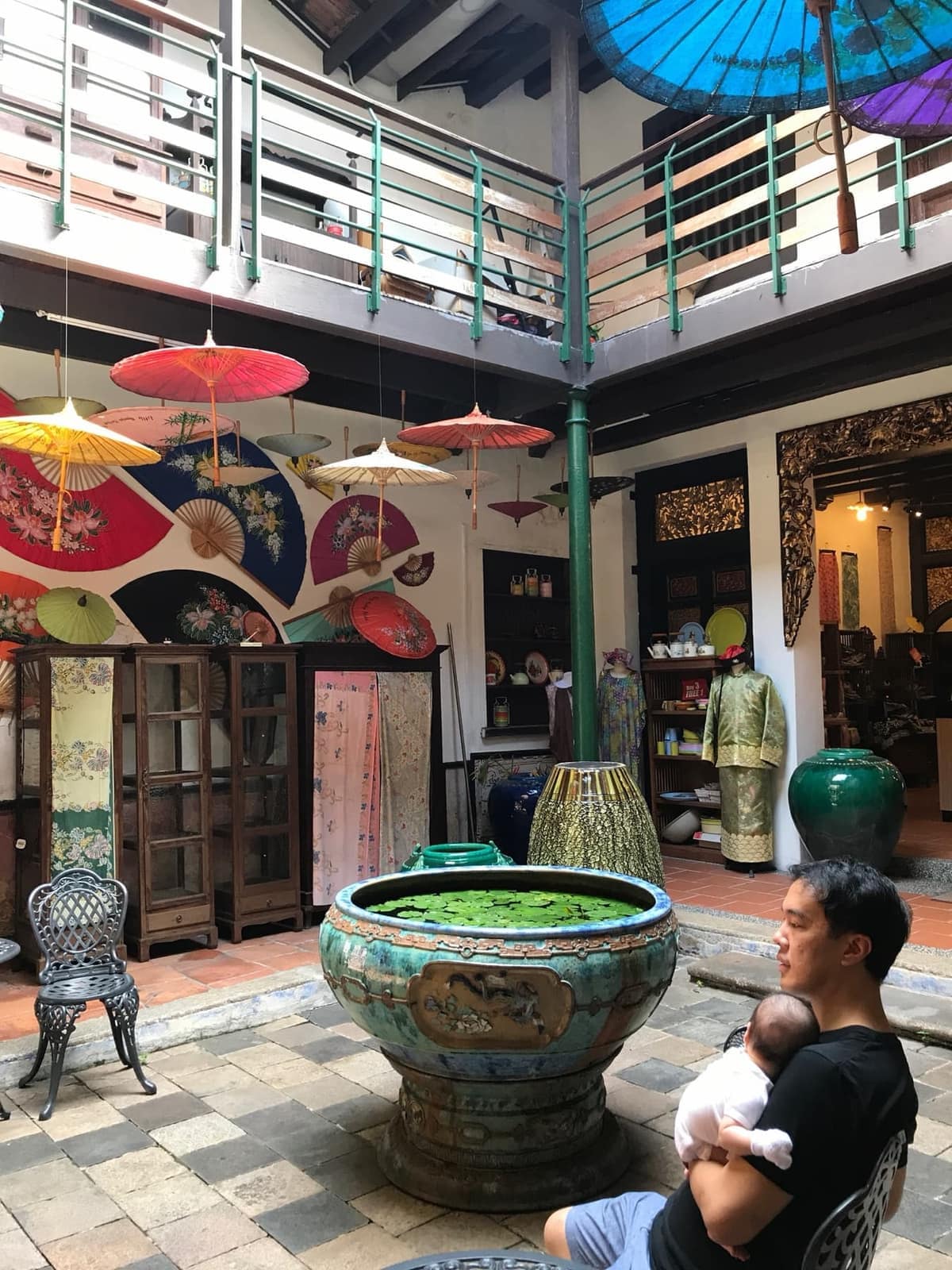 Philip holding baby Sophie in a Malacca courtyard decorated with umbrellas and ceramics