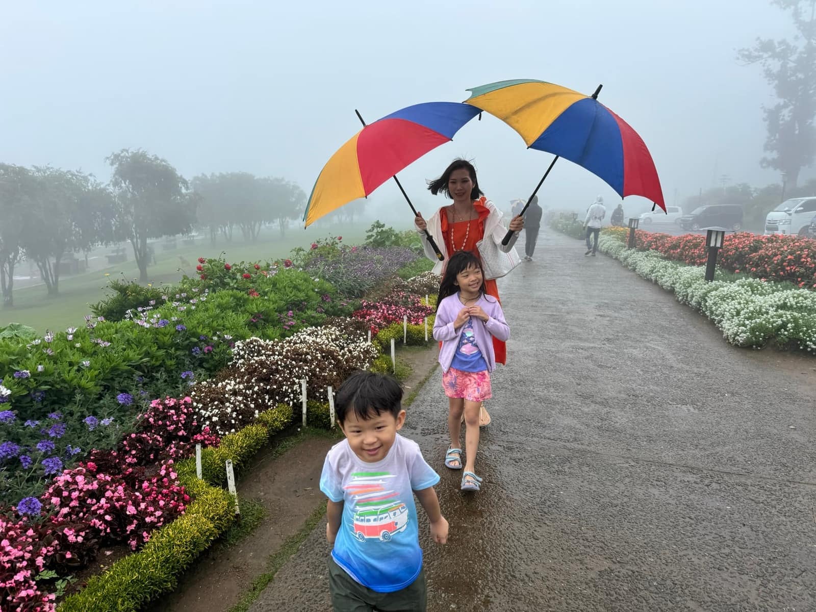 Vanessa and the children walking through a misty highland garden beneath colourful umbrellas