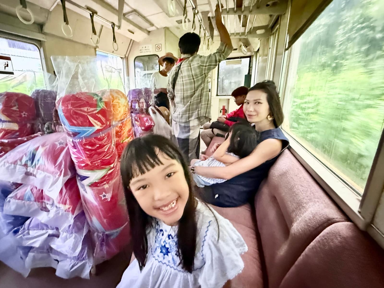 Sophie seated inside a Yangon train carriage with pillows, bolsters and bedding behind her